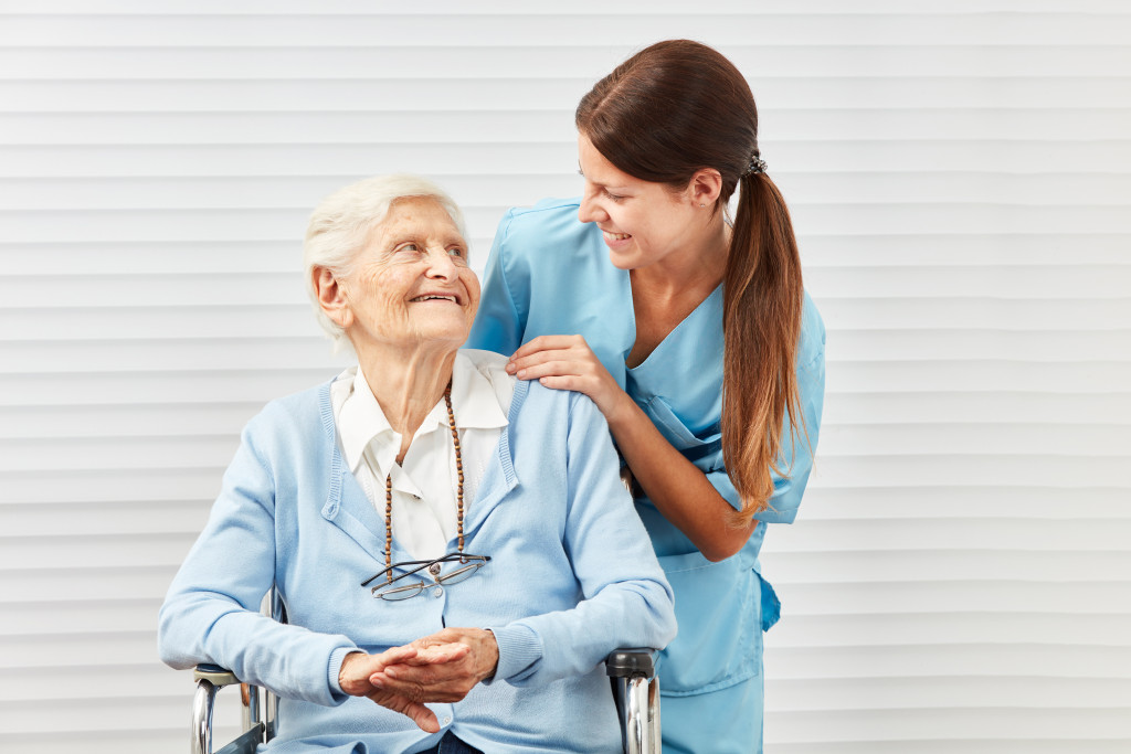 A caregiver and an older woman on a wheelchair looking and smiling at each other
