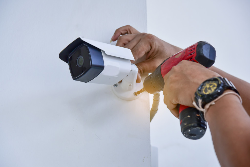 A person installing a security camera on a wall using a hand drill