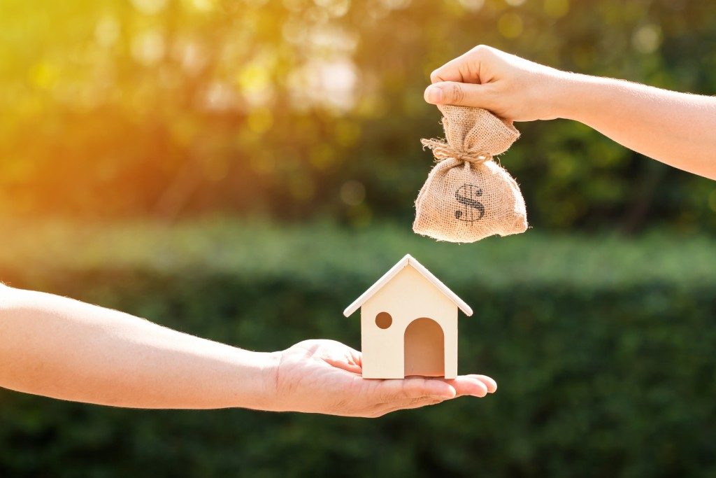 Loans for real estate concept, a man and a women hand holding a money bag and a model home put together in the public park.