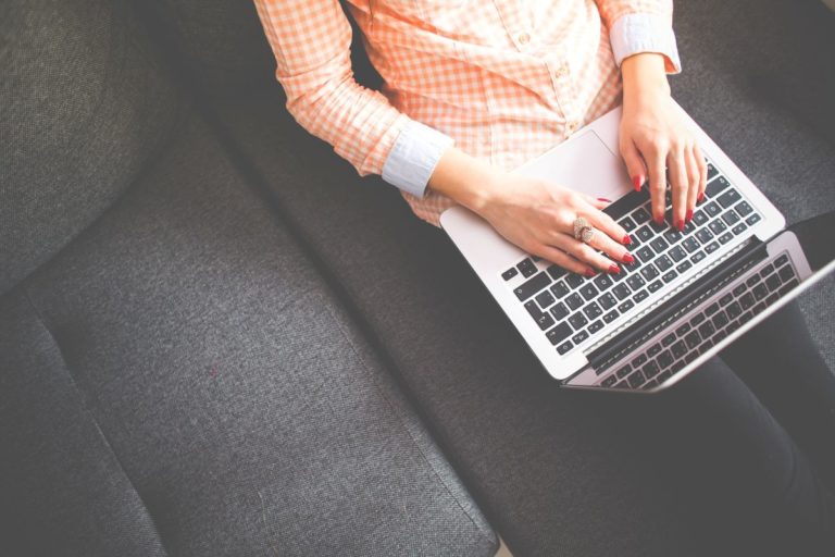 woman sitting on couch working remotely using her laptop