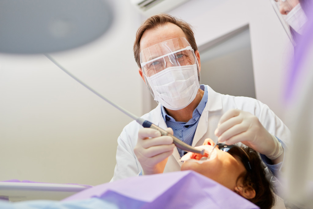 Dentist with protective mask and drill while treating patient in the dental office