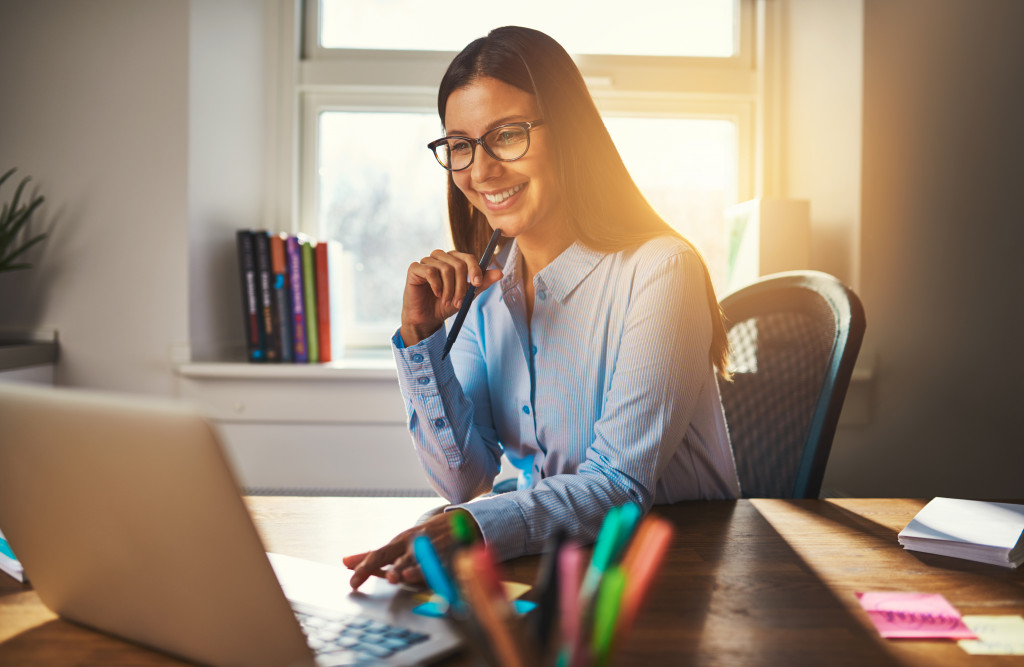 a woman in her workspace smiling as sun shines from outside