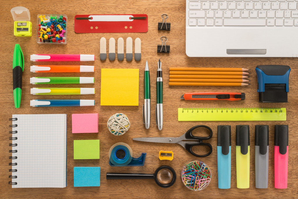 Notebook, pens, pencils, highlighters, erasers, clips, and other office supplies on a table.