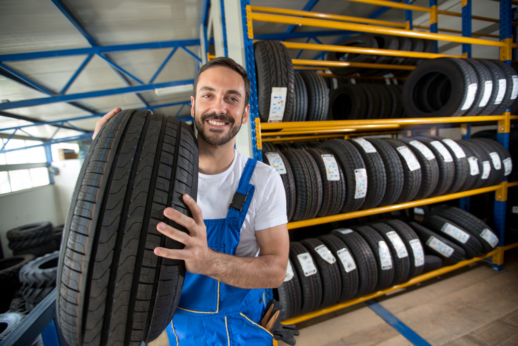 a man smiling while holding a tire in a tire shop