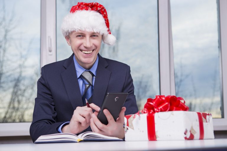 A businessman wearing a Santa hat while working on an office desk with a gift