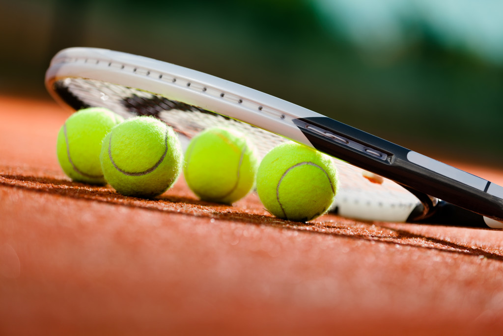 Tennis racket and tennis balls on a clay court.