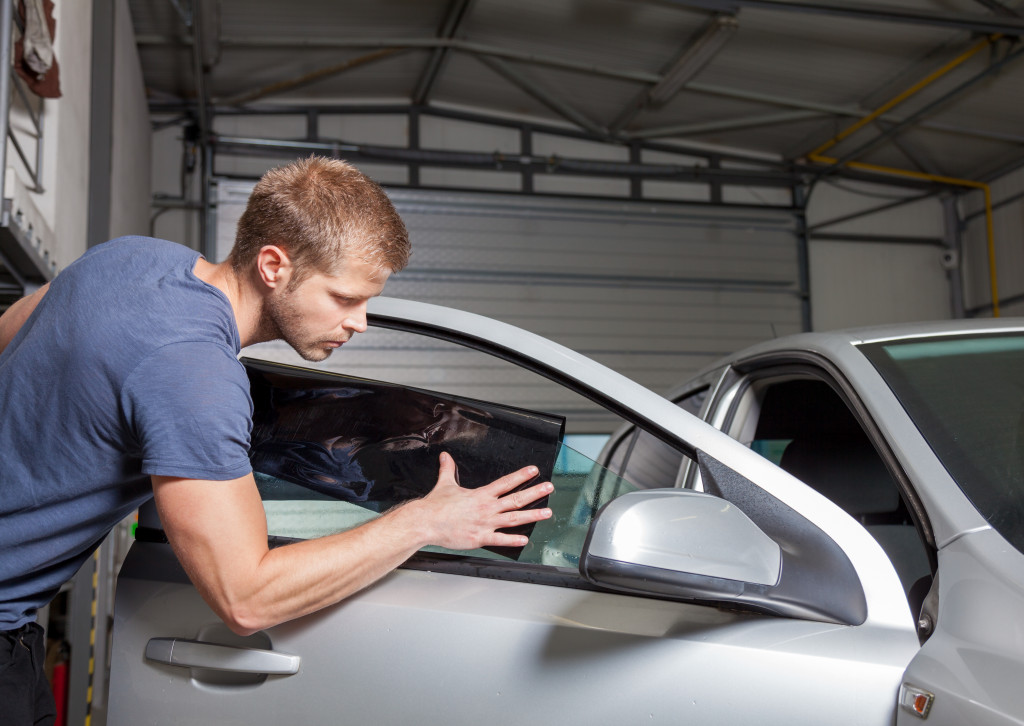 A man applying tint on a car window in a garage