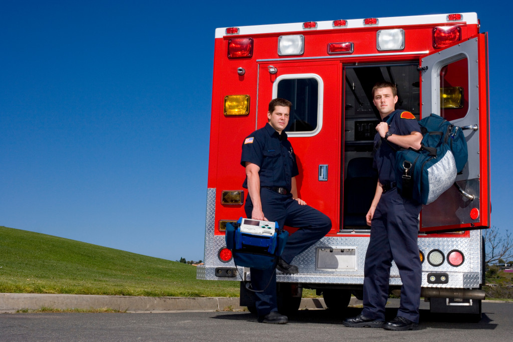 2 EMTs carrying their medical supplies on the back of an ambulance
