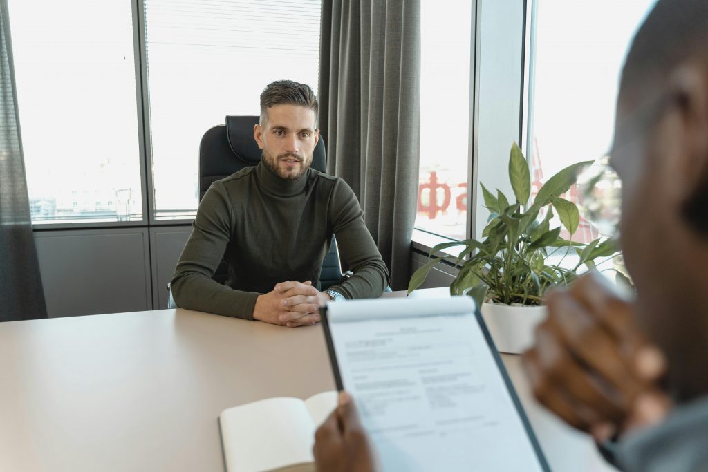 man wearing a turtleneck in a job interview across a desk from an interviewer