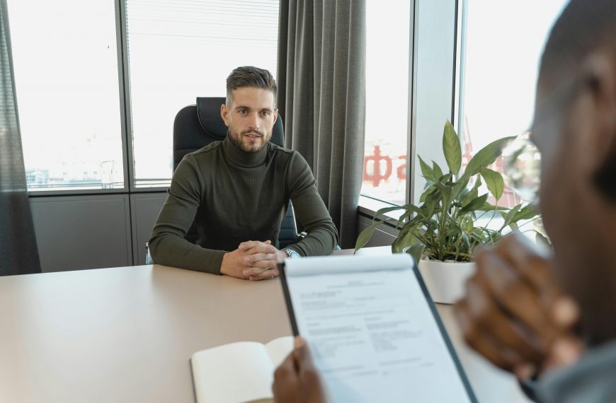 man wearing a turtleneck in a job interview across a desk from an interviewer